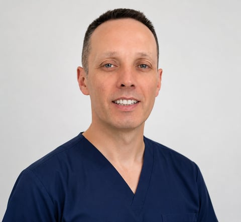 Professional headshot of a smiling man with short dark hair wearing a dark blue v-neck shirt against a white background
